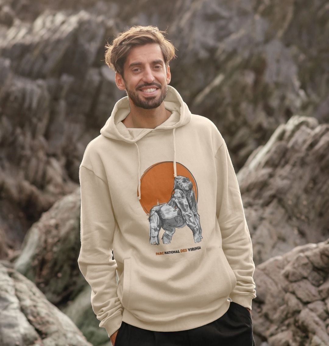 A Man wearing a beige Ndakasi Men's Hoodie against a rocky background