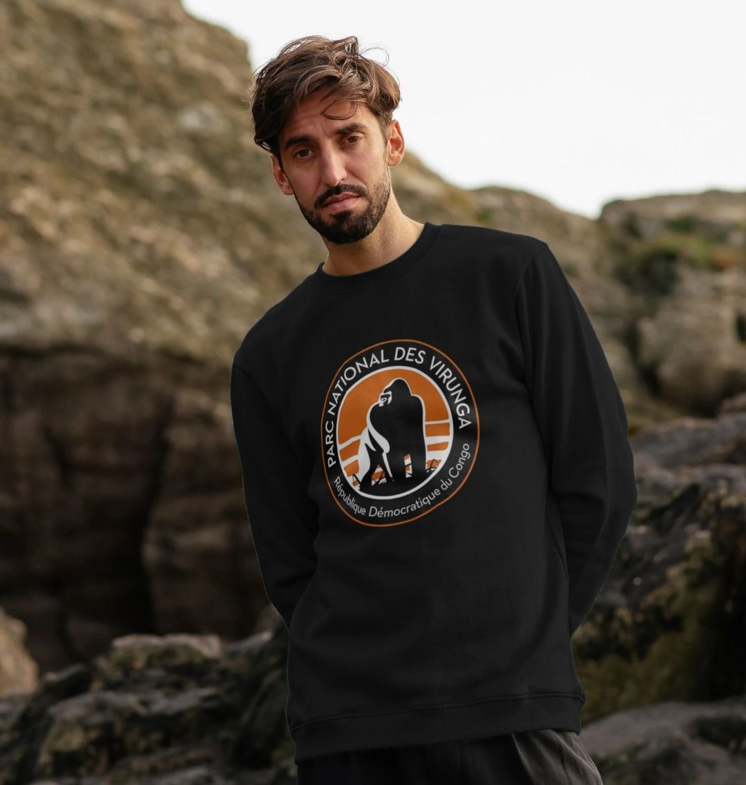 A man wearing a black Virunga Logo Men's Sweater in front of rocky terrain