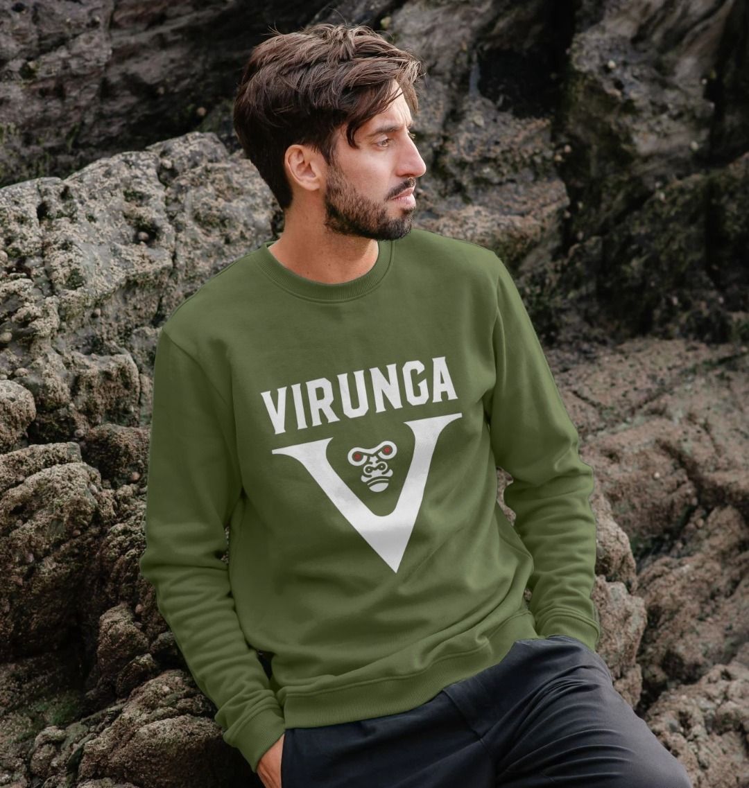 A man wearing a khaki V for Virunga Men's sweater sits on rocks.
