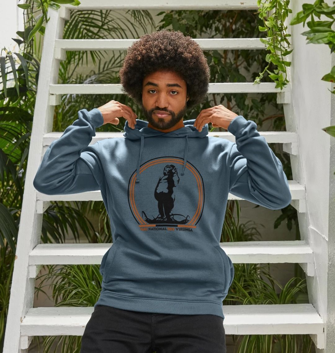 A man wearing a navy blue Take A Stand Men's Hoodie, standing in front of a white ladder and greenery.