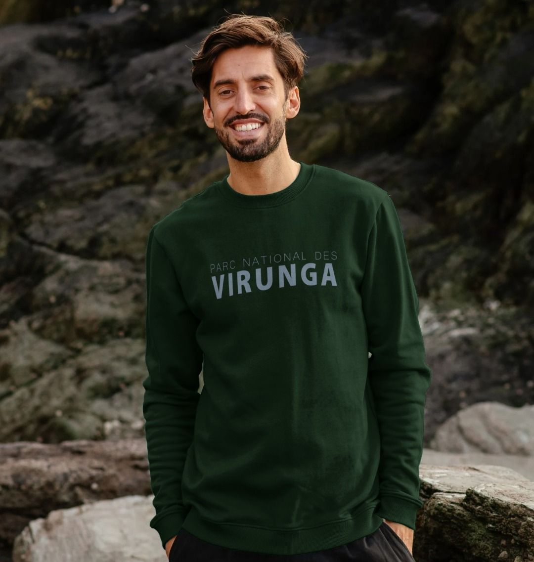 Man wearing an evergreen Parc National des Virunga Men's Sweater, standing against a rocky background.
