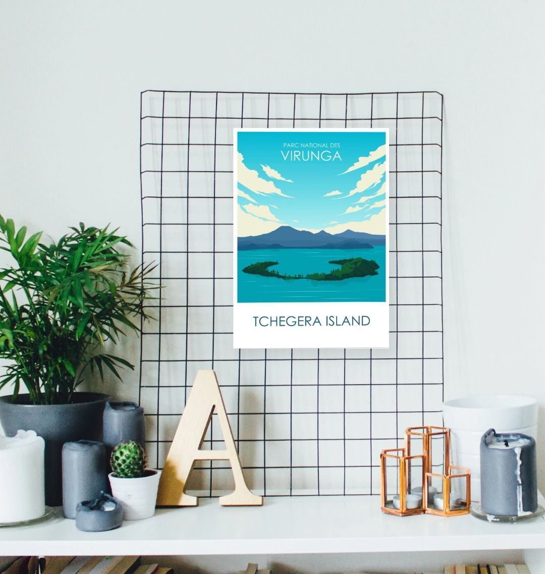 A poster featuring Tchegera Island with a blue sky and greenery, displayed on a wall above a decorative letter 'A', with a plant and a framed picture in the background.