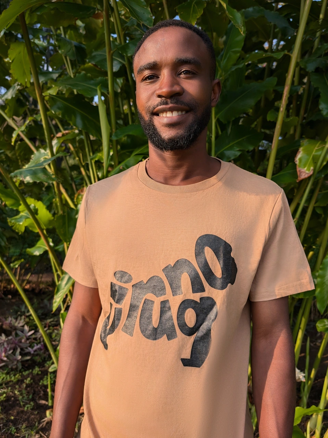 Man Wearing a Sand Gorilla Emblem Men's T-shirt standing in front of green foliage