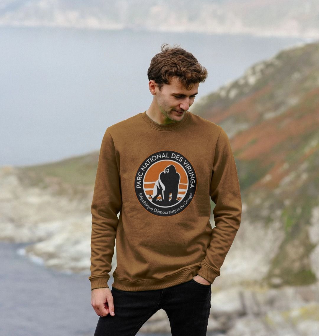 A Man wearing a sage Virunga Logo Men's Sweater in front of a mountainous landscape