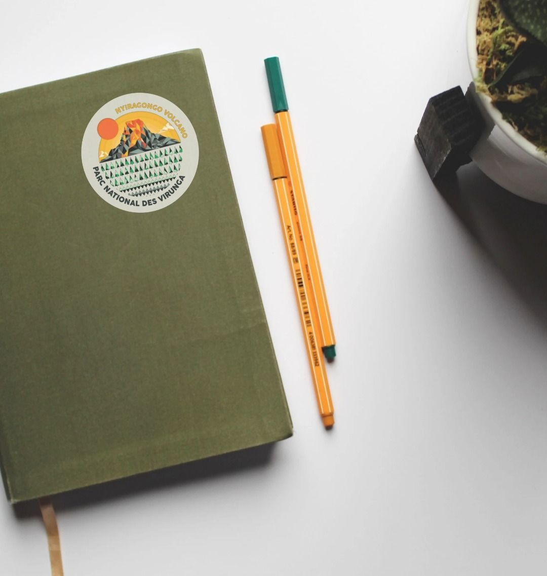 A Nyiragongo Volcano Sticker, placed on a green notebook which is itself on a wooden table.