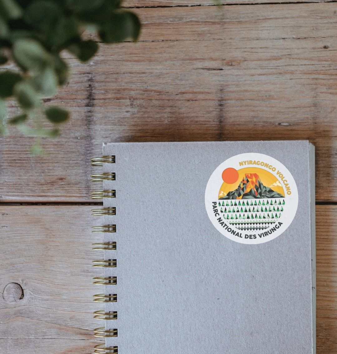 A Nyiragongo Volcano Sticker, placed on a notebook which is itself on a wooden table.