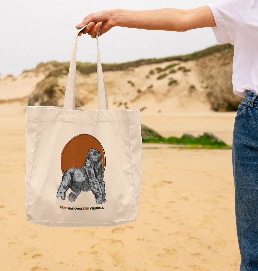 A person holding a beige shopper tote bag with a graphic design of a mountain gorilla and the text 'Ndakasi, Virunga'.