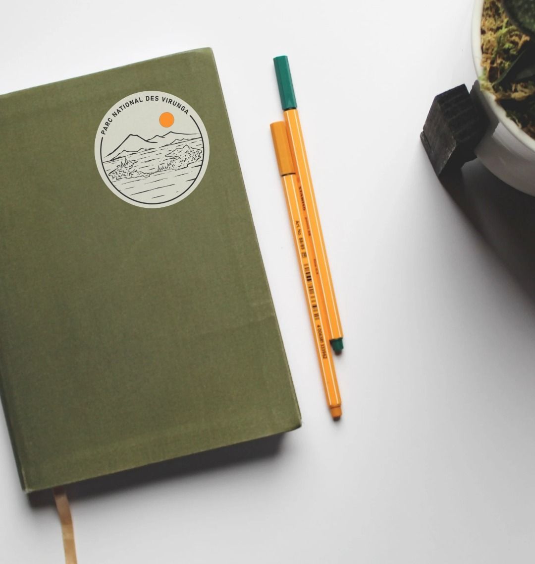 A Tchegera Island Sticker placed on a green notebook which is itself on a white table.