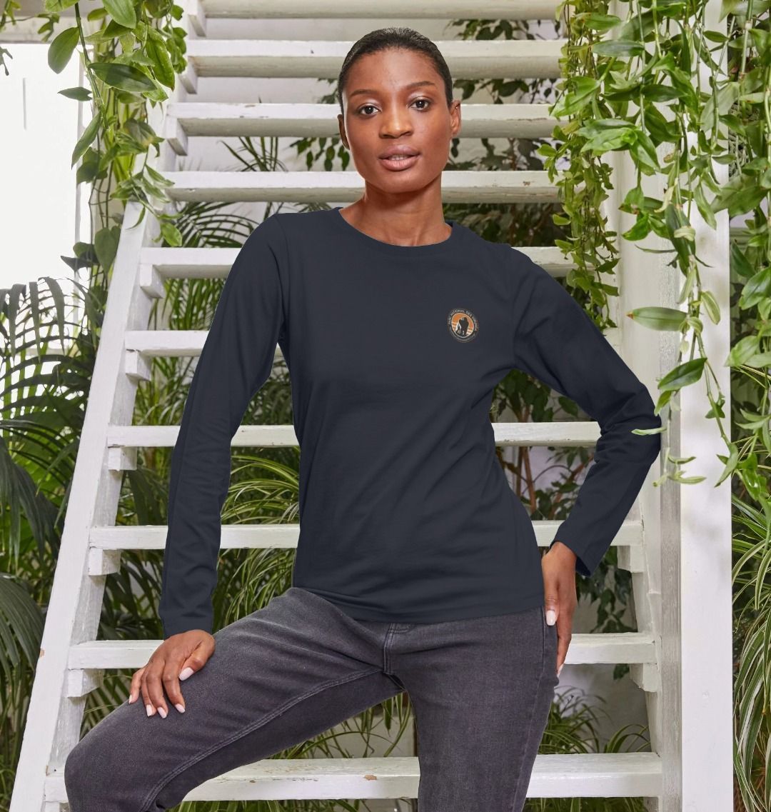 A woman wearing a Virunga Pocket Logo Women's Long Sleeve T-shirt standing on a staircase surrounded by green foliage.