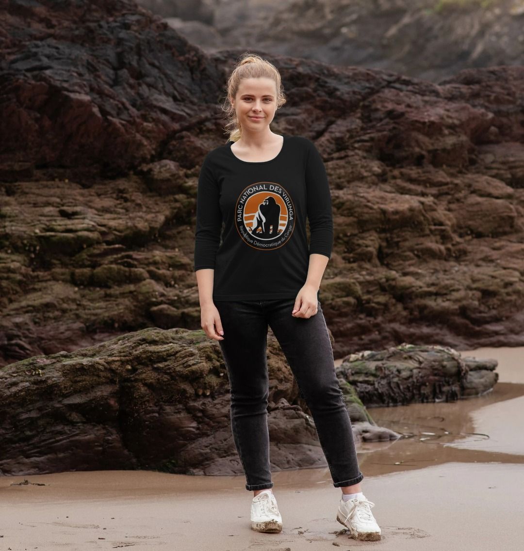 A woman standing on a beach wearing a black 3/4 sleeve t-shirt , and black pants.