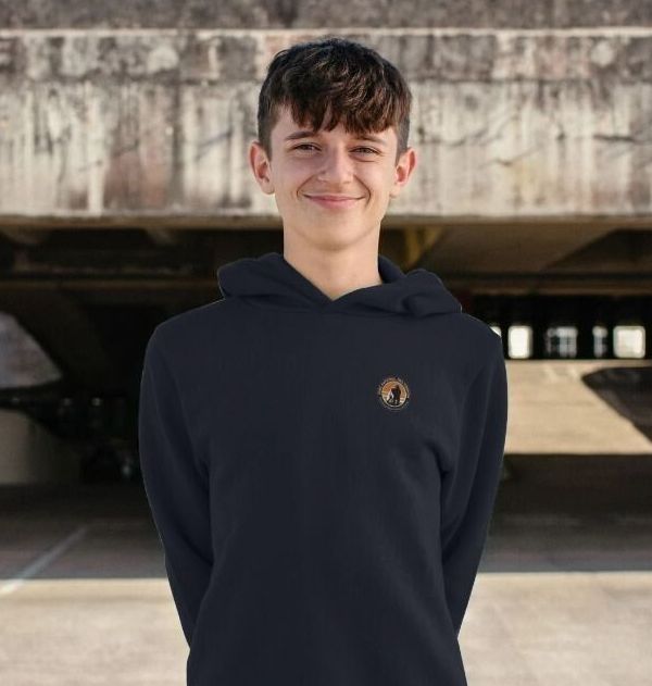A kid wearing a black Virunga Pocket Logo Kids Hoodie, standing in a parking structure.