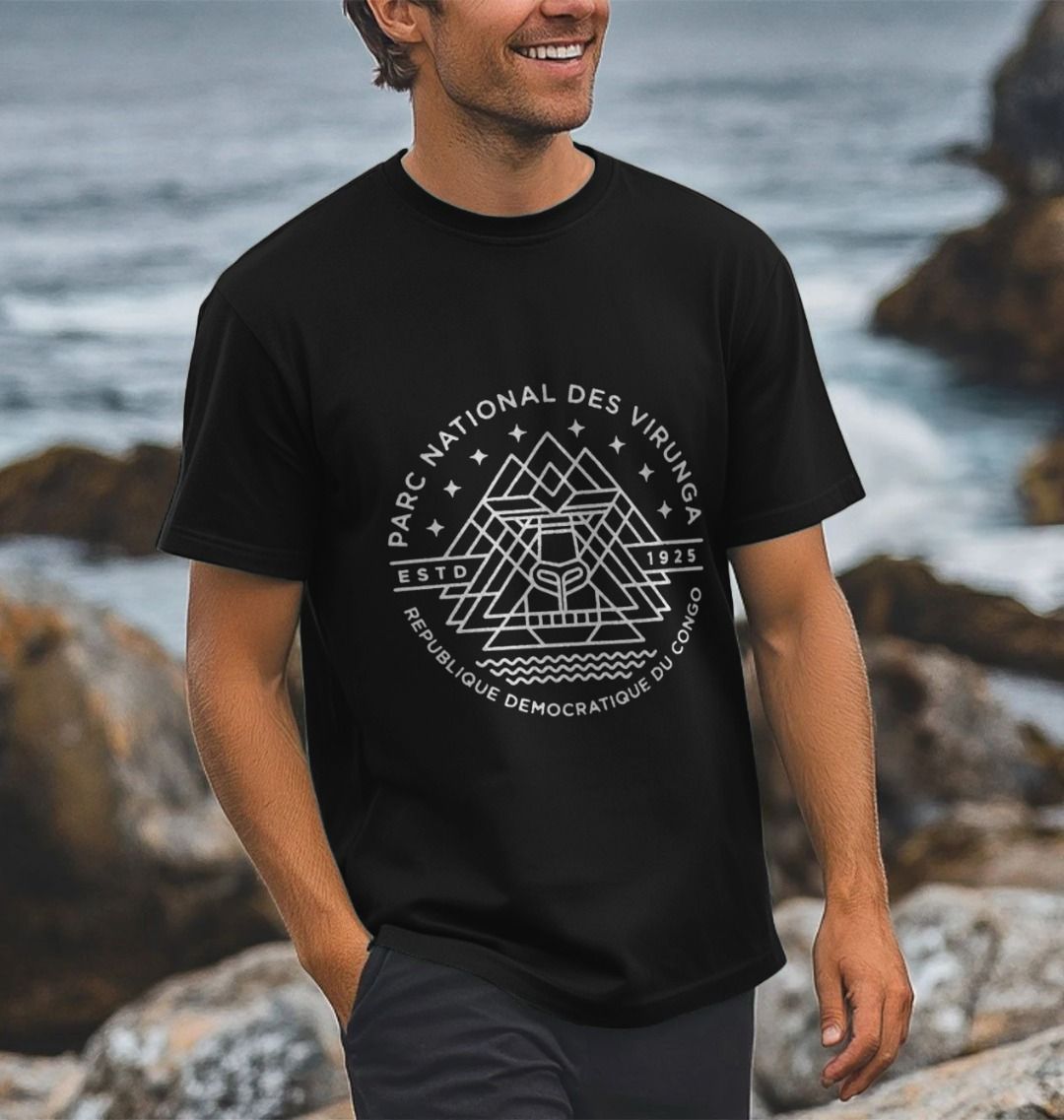 A man wearing a black Virunga Emblem Men's T-shirt standing near a rocky coastline.