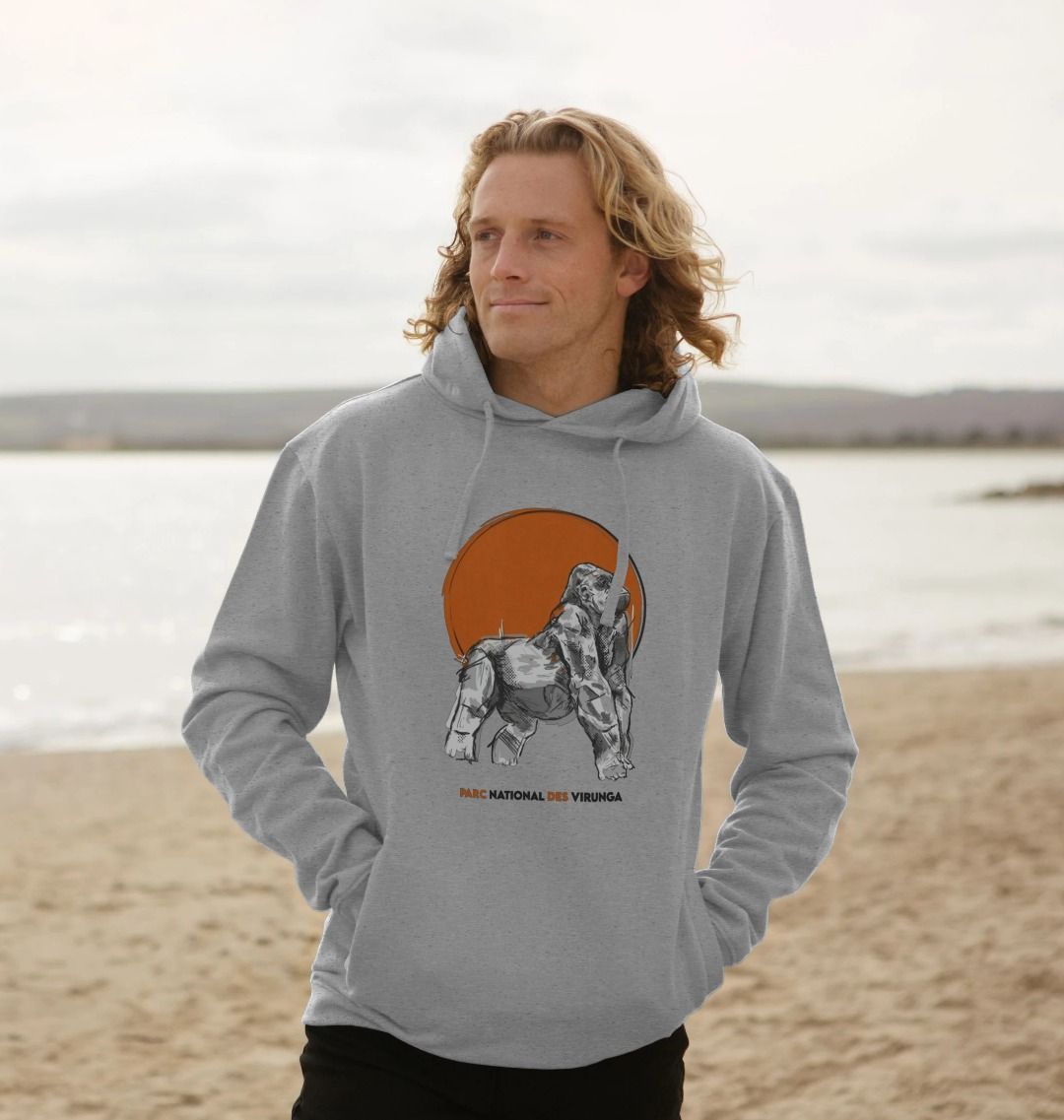 A man wearing a light heather Ndakasi Men's Hoodie on a plage