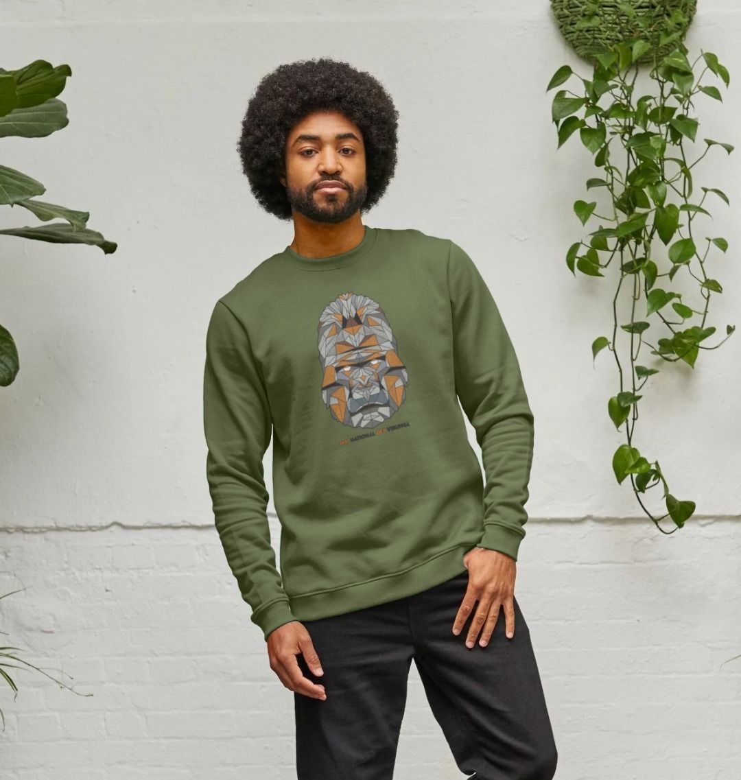 A man wearing an evergreen Gorilla Face Men's Sweater, standing against a white wall with plants.