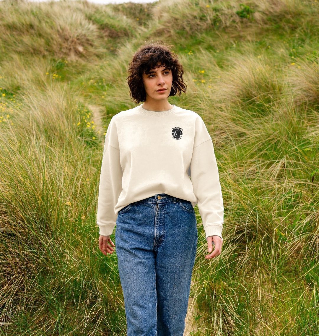 A person standing in an outdoor setting wearing an oat Gorilla Pocket Logo Oversized Jumper paired with blue jeans.
