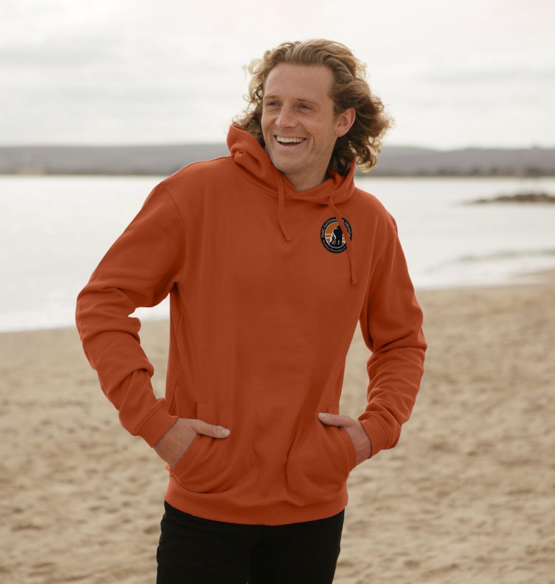 A Man Wearing a Rust Virunga Pocket Logo Men's Hoodie, standing on a beach.
