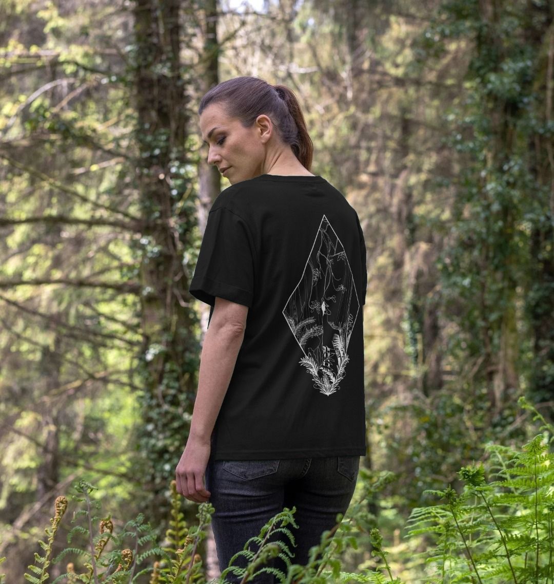 A woman standing in a forest setting, wearing a black Women's Okapi T-shirt.