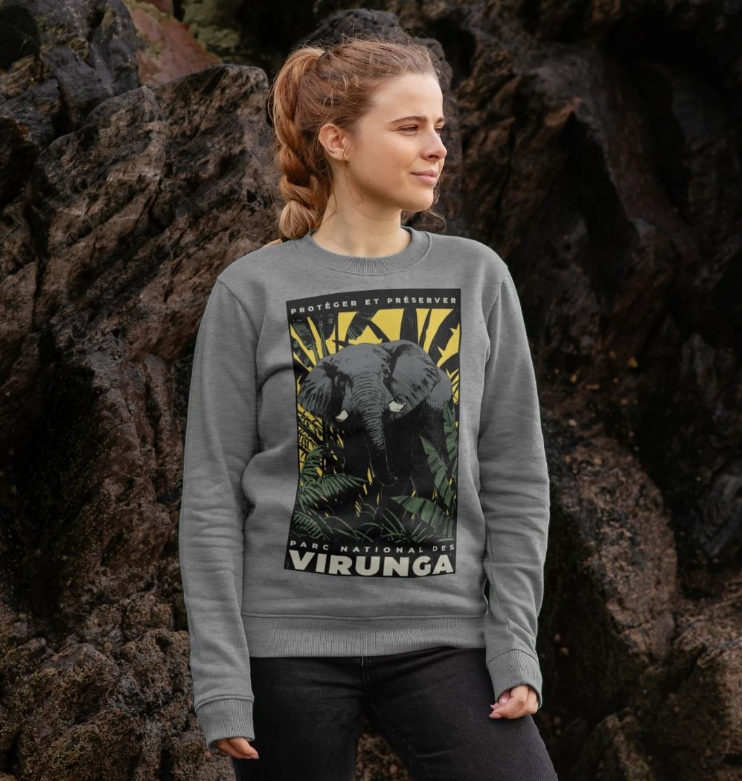 A woman standing in a front of stones, wearing a light heather African Yellow Print Women's Sweater.