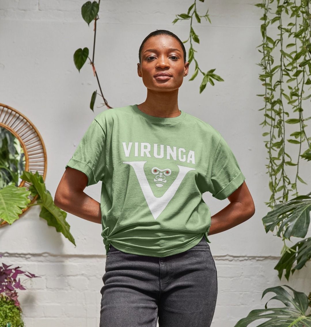 A woman standing in a room with plants, wearing a sage V for Virunga Women's Relaxed Tee