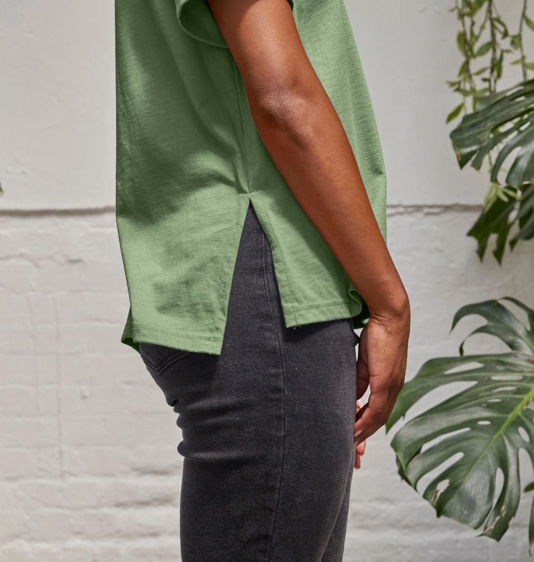 A woman standing in a room with plants, wearing a sage V for Virunga Women's Relaxed Tee