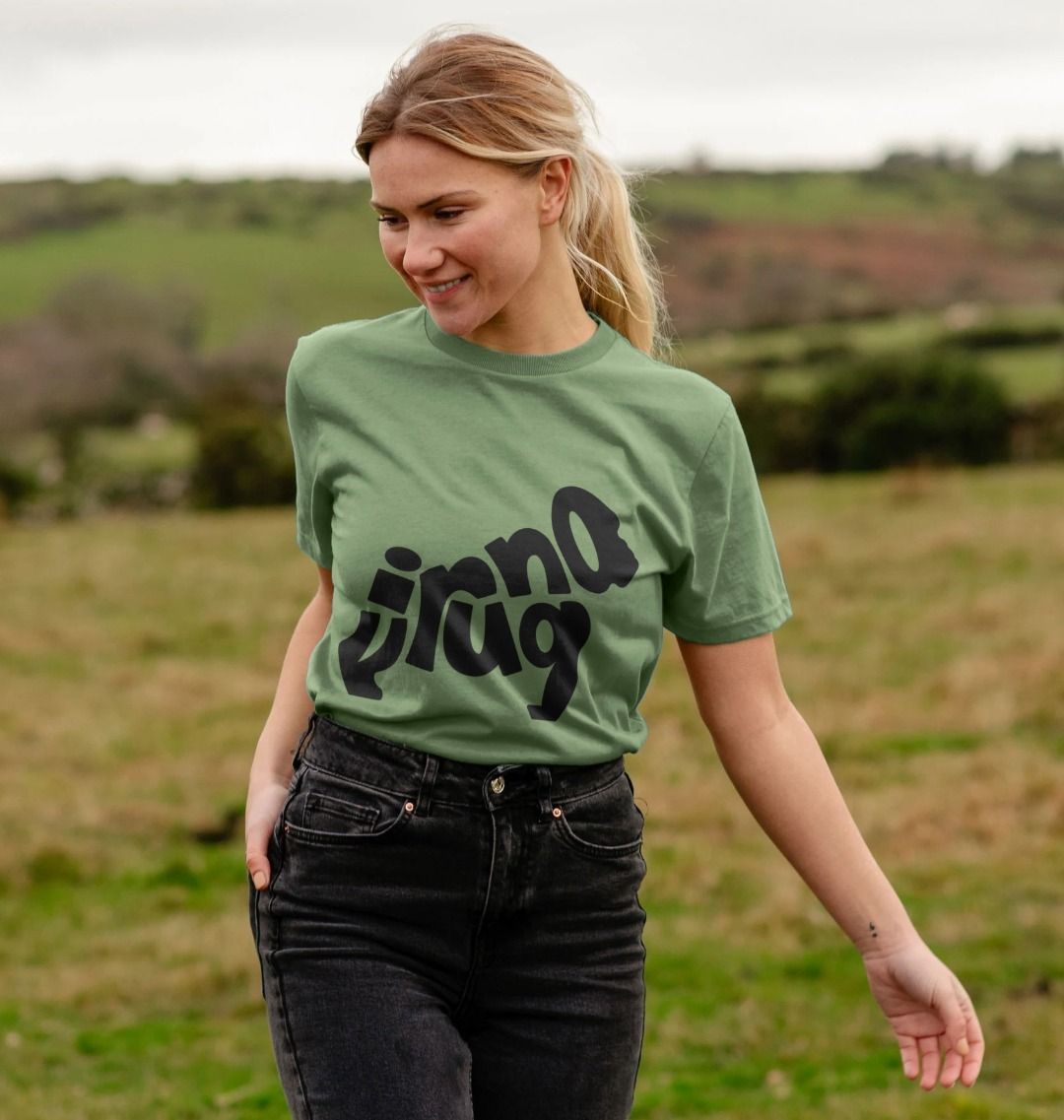 A woman wearing a Sage Gorilla Emblem Women's T-shirt standing in a field.