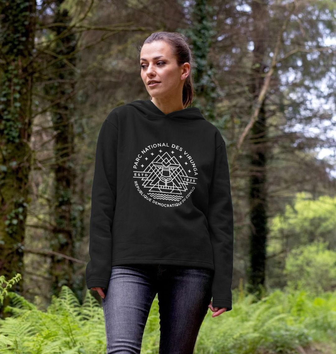 A woman wearing a black Virunga Emblem Women's Hoodie, standing in the forest.
