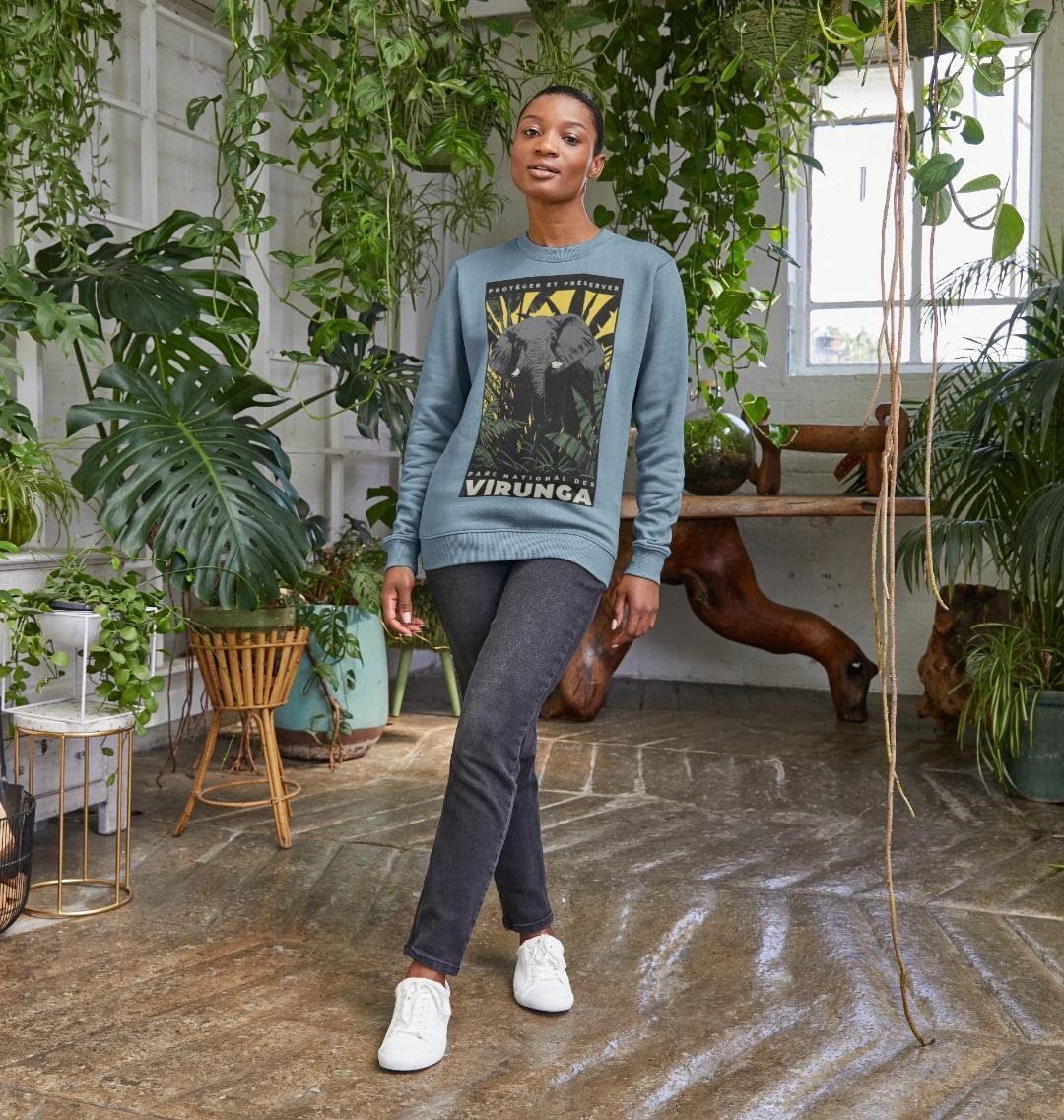 A woman standing in a beautifully decorated indoor space with plants, wearing a stone blue African Yellow Print Women's Sweater.