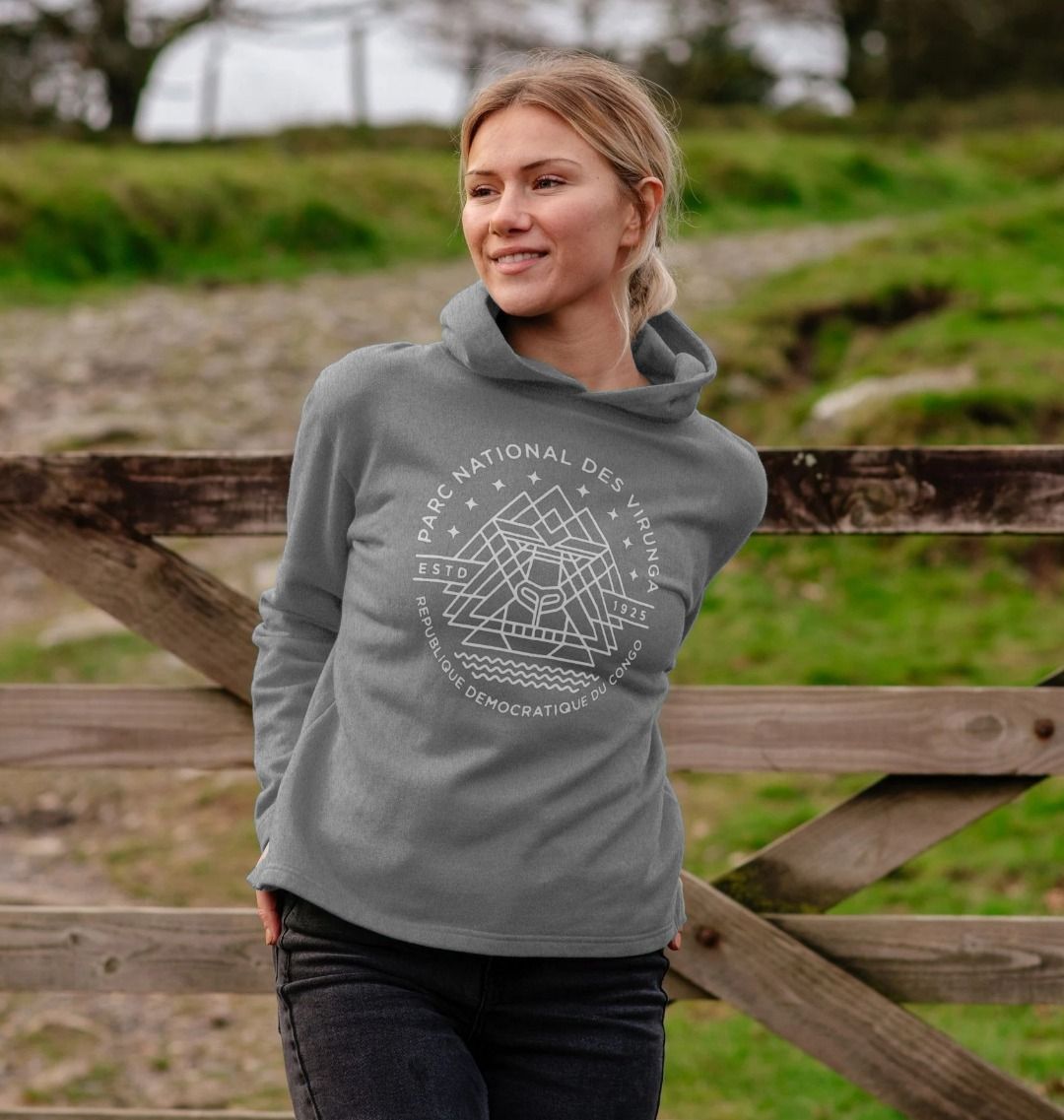 A woman wearing an athletic grey Virunga Emblem Women's Hoodie , standing near a wooden fence.