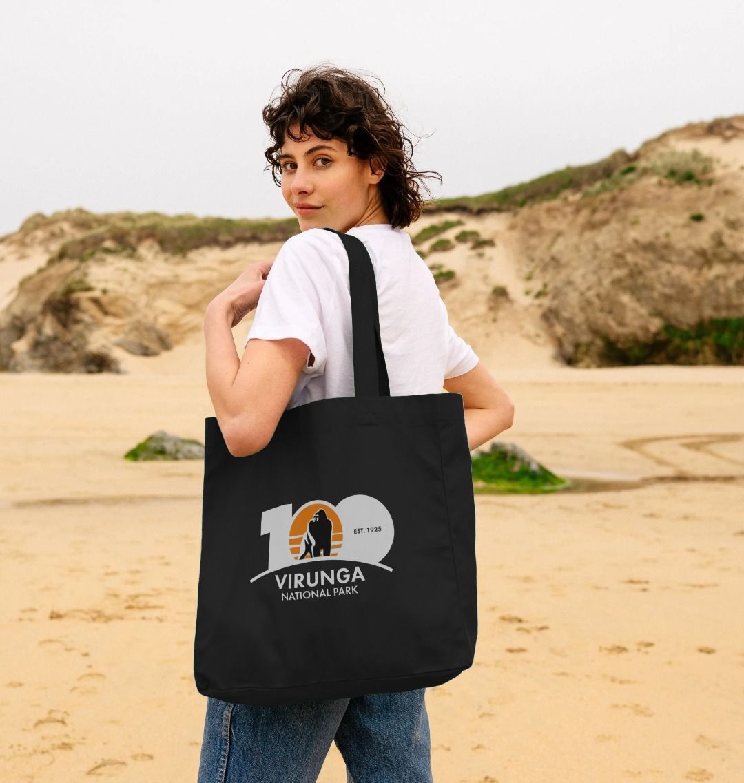 A person standing on a beach holding a black Virunga 100 Shopper Bag