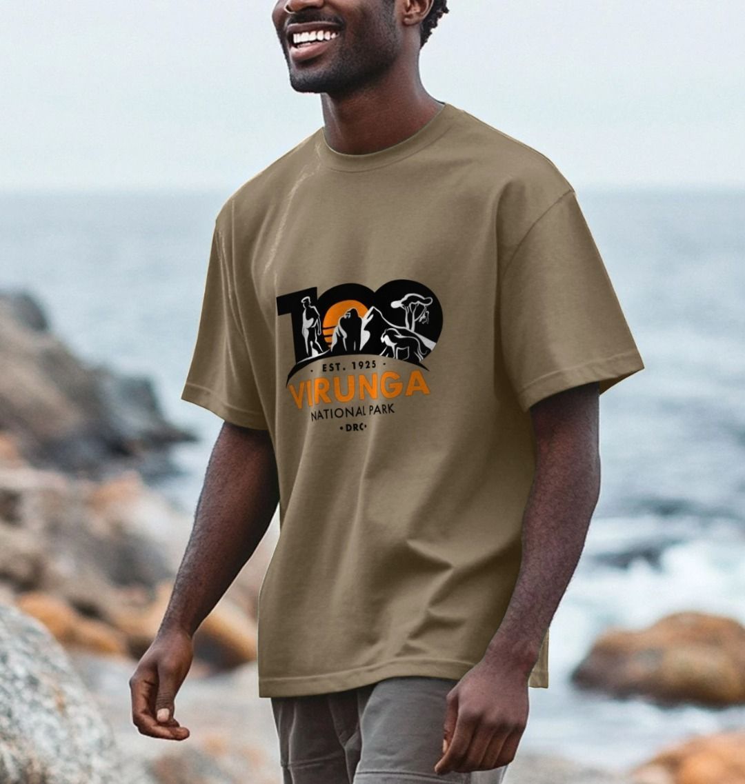 A man standing by the sea wearing a chocolate  Virunga 100 Men's Oversized T-shirt.