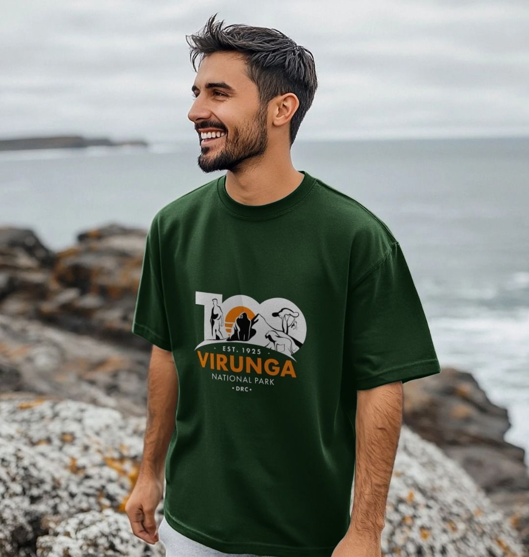 A man standing by the sea wearing a green Virunga 100 Men's Oversize T-shirt