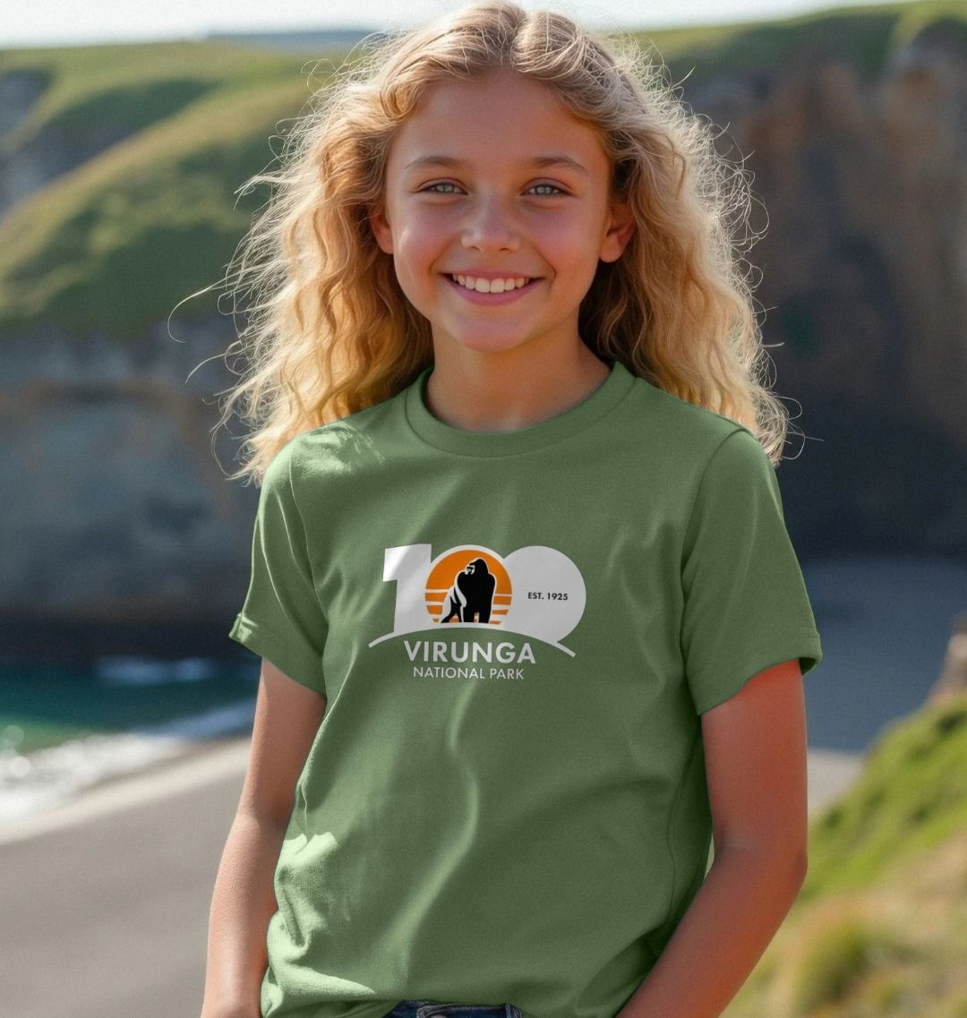 A child standing by the sea wearing a green Virunga 100 Kids T-shirt.