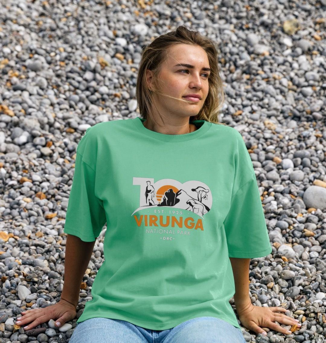 A white girl wearing a green Virunga 100 Women's Oversize T-shirt sitting on pebbles.