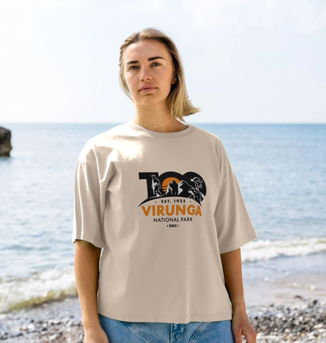 A woman standing by the sea wearing an oat Virunga 100 Women's Oversized T-shirt.