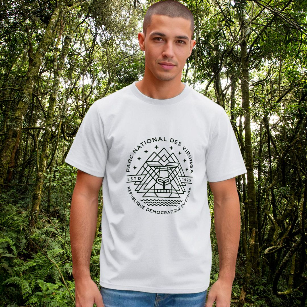 A man wearing a white Men's Virunga Emblem t-shirt, standing in a lush green forest of Virunga National Park.