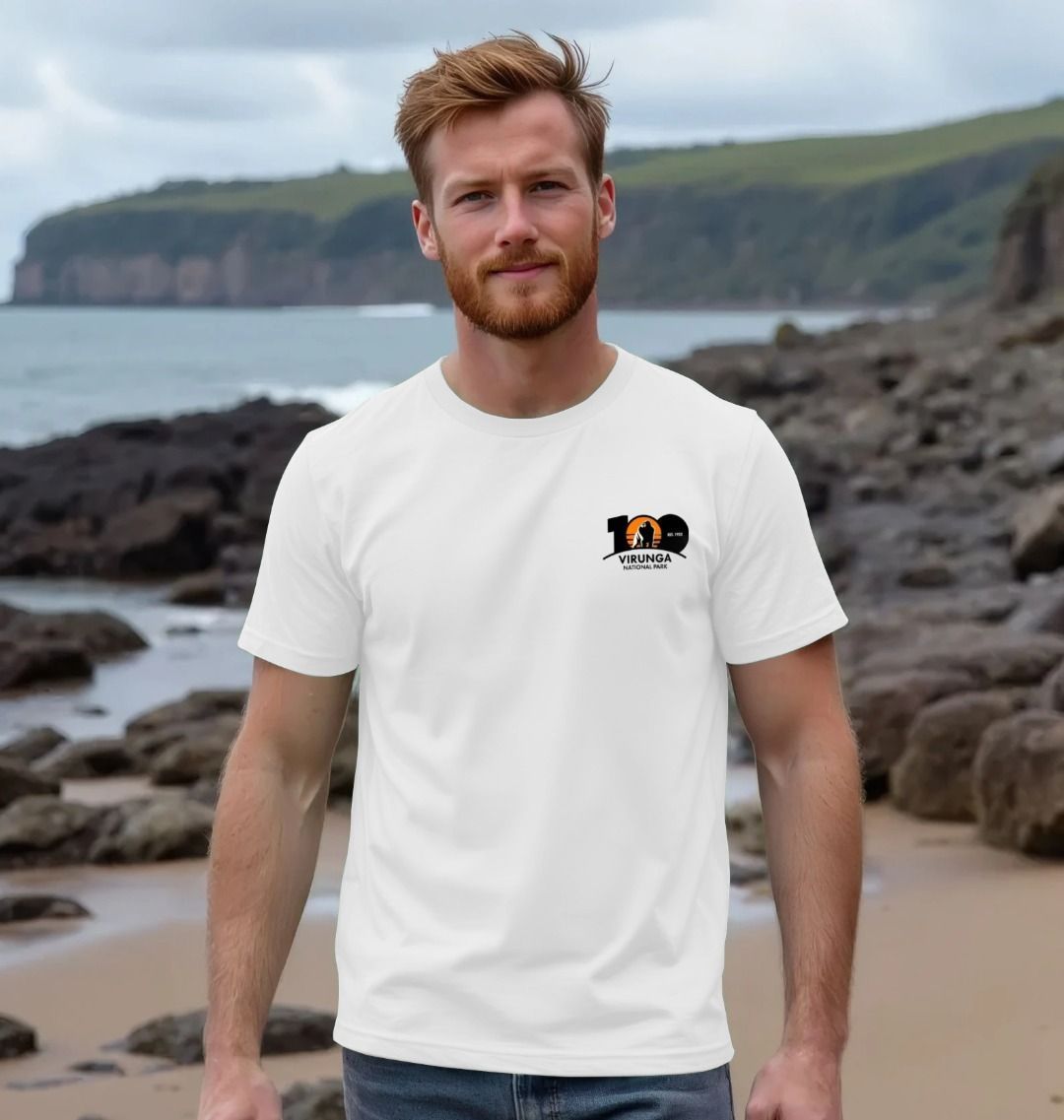A man standing on a beach wearing a white Virunga 100 Men's T-shirt.